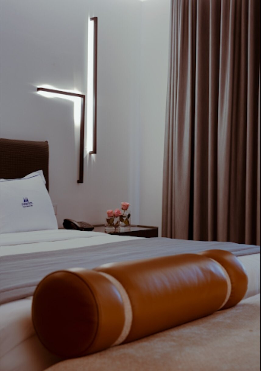 Maritim Collection Marina Bay Hotel - bed with a tan leather bolster cushion and wall lights, Vlora