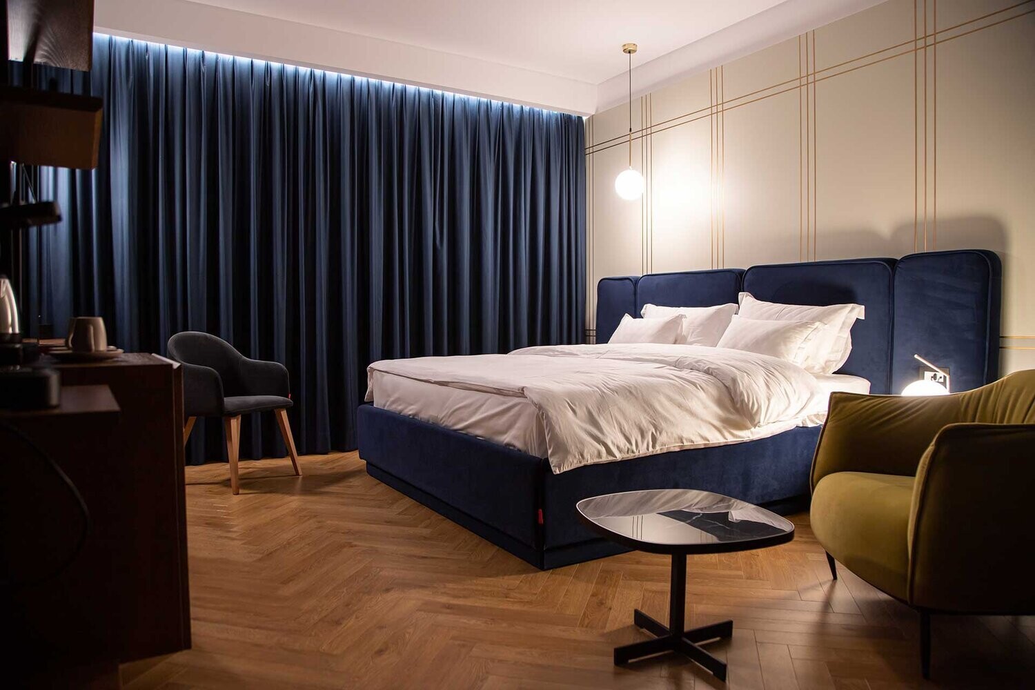 Moncaffe Hotel - bedroom with a navy bed, mustard armchair and pendant lights, Albania